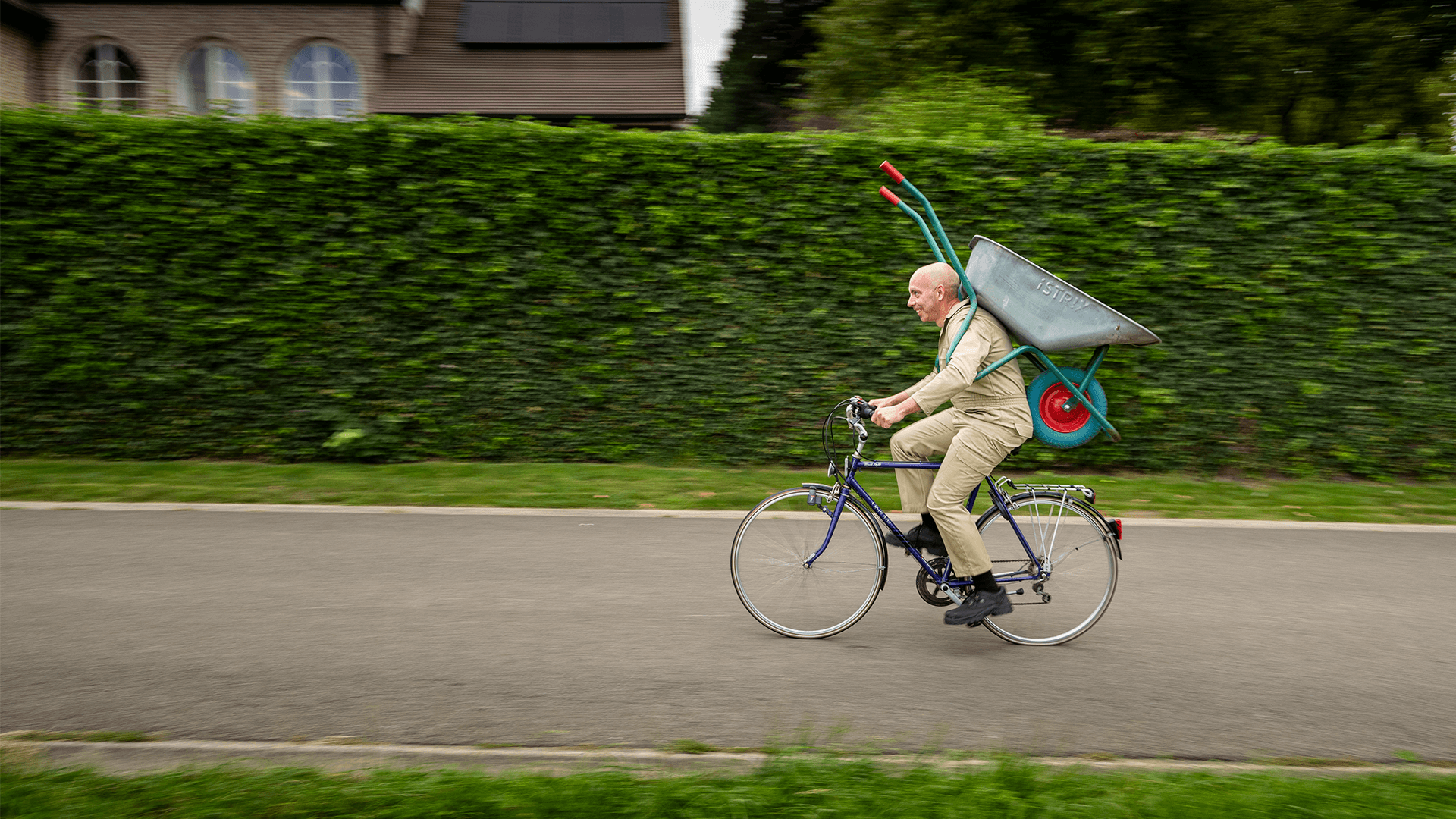 Man op fiets met kruiwagen op rug